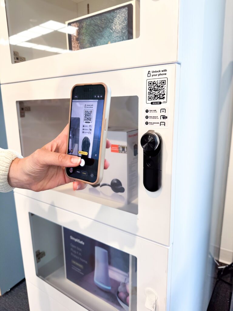 Un comprador escanea un código QR de acceso autónomo para clientes en la puerta de una vitrina de seguridad equipada con una cerradura « InVue » (LIVE ).