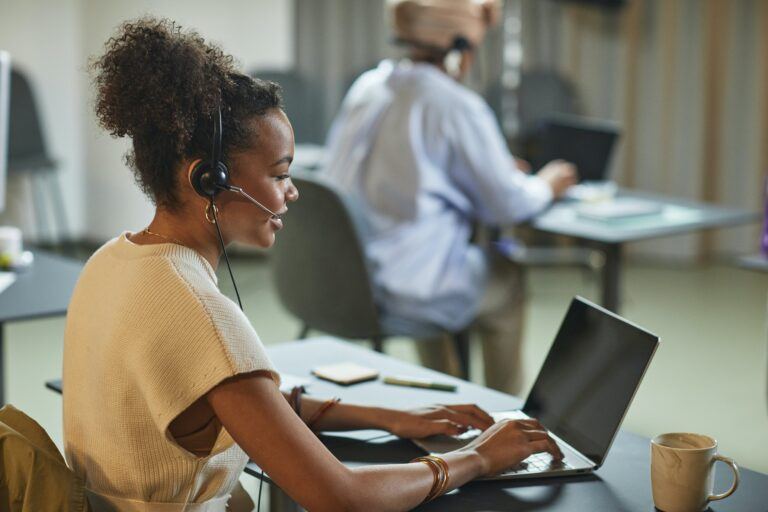 Mujer sentada ante un portátil con auriculares de atención al cliente