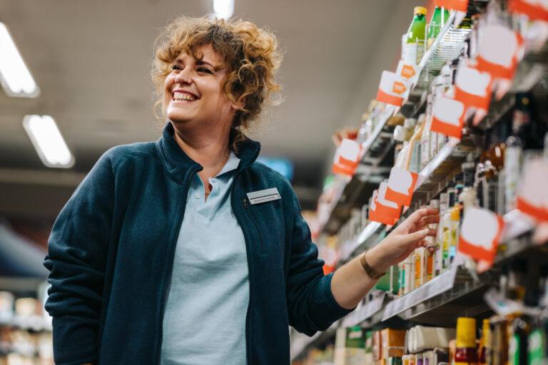 Mujer de negocios segura de sí misma junto a los estantes y sonriendo en un supermercado. Mujer gerente en una tienda de comestibles.